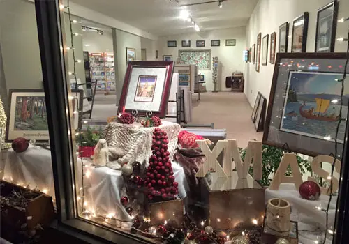 A decorated shop window displays framed art and Christmas ornaments.