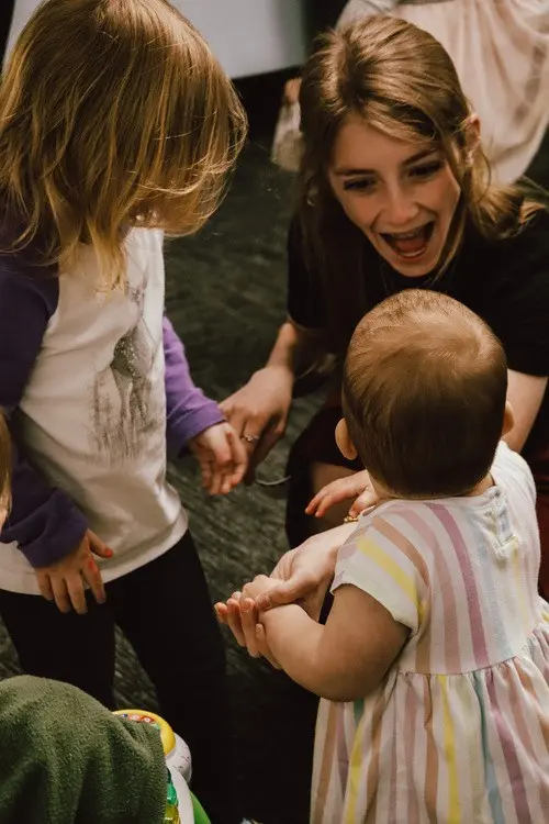 A woman smiles while interacting with two young children.
