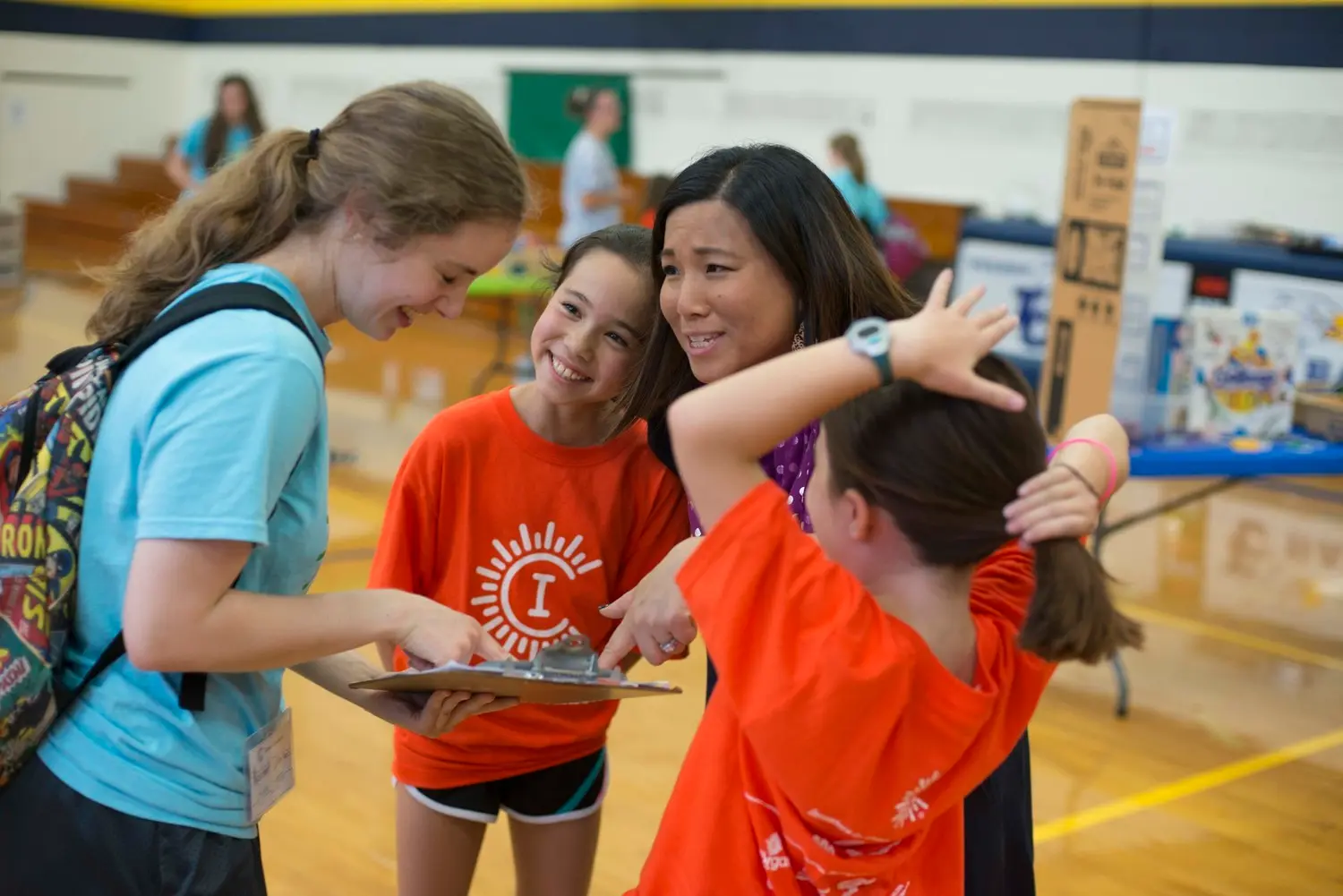 A Camp Invention Instructor and Leadership Intern chat about a STEM activity as two campers smile nearby