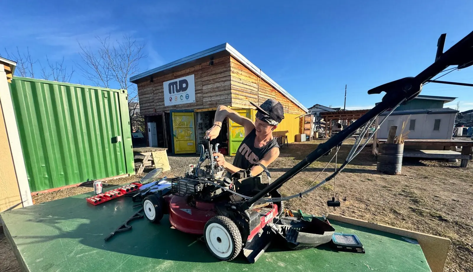 A young person is working on repairing a lawnmower outdoors.