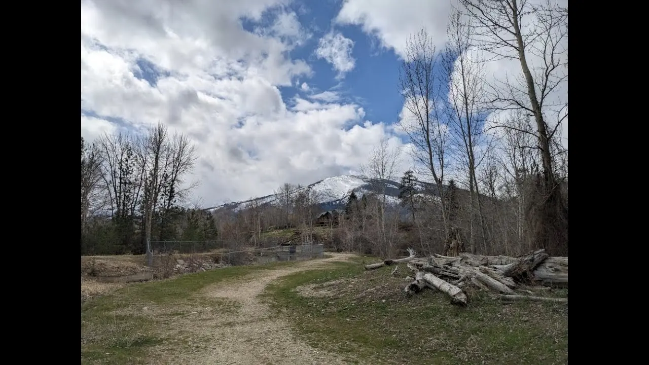 A dirt trail leads toward a snow-covered mountain under a cloudy sky.