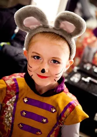 A child wearing mouse ears and face paint looks at the camera.