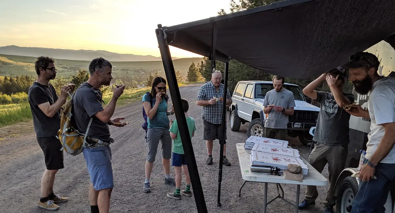 A group of people enjoy a meal together outdoors at sunset.