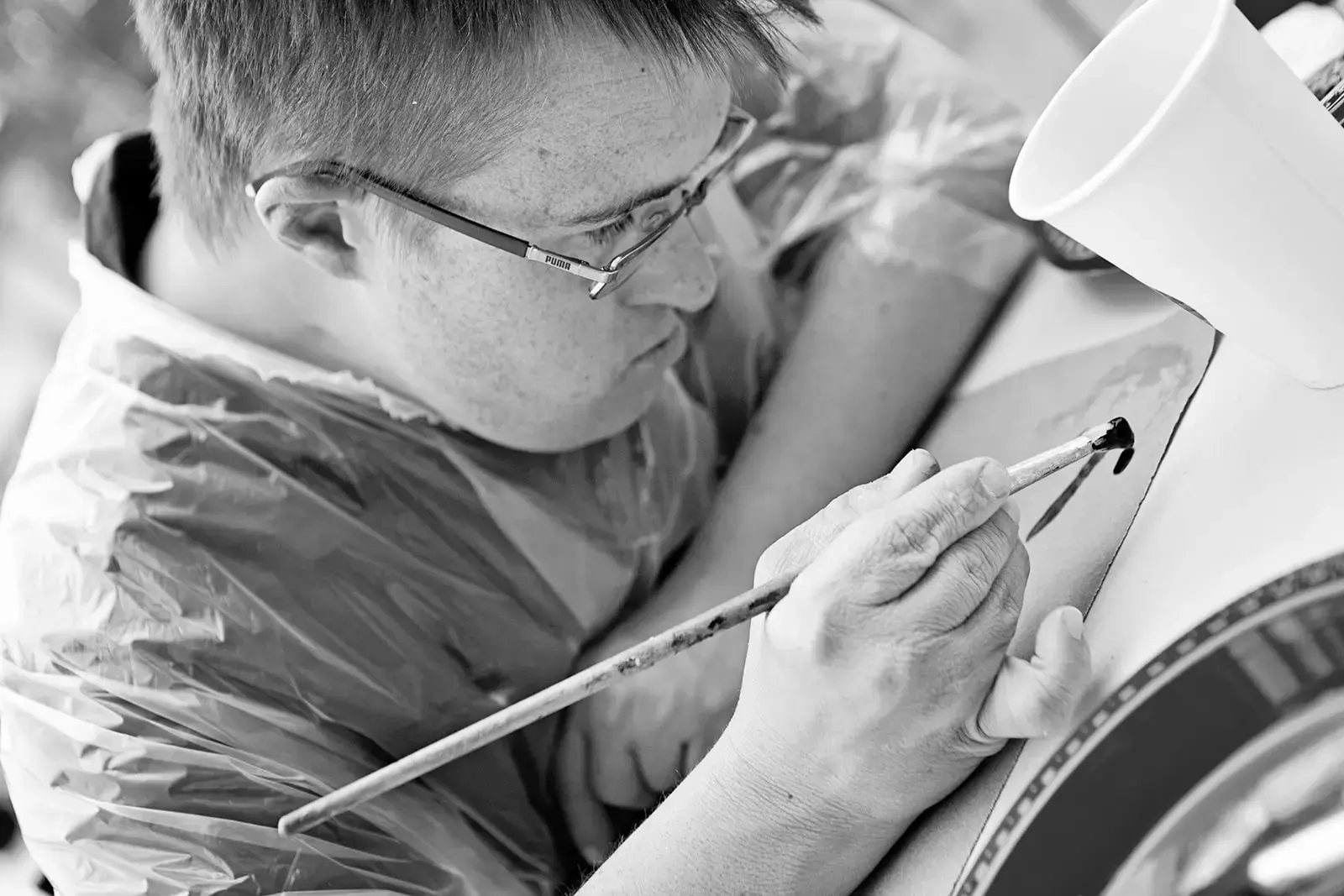 A person wearing glasses and a plastic apron paints on a surface with a brush.