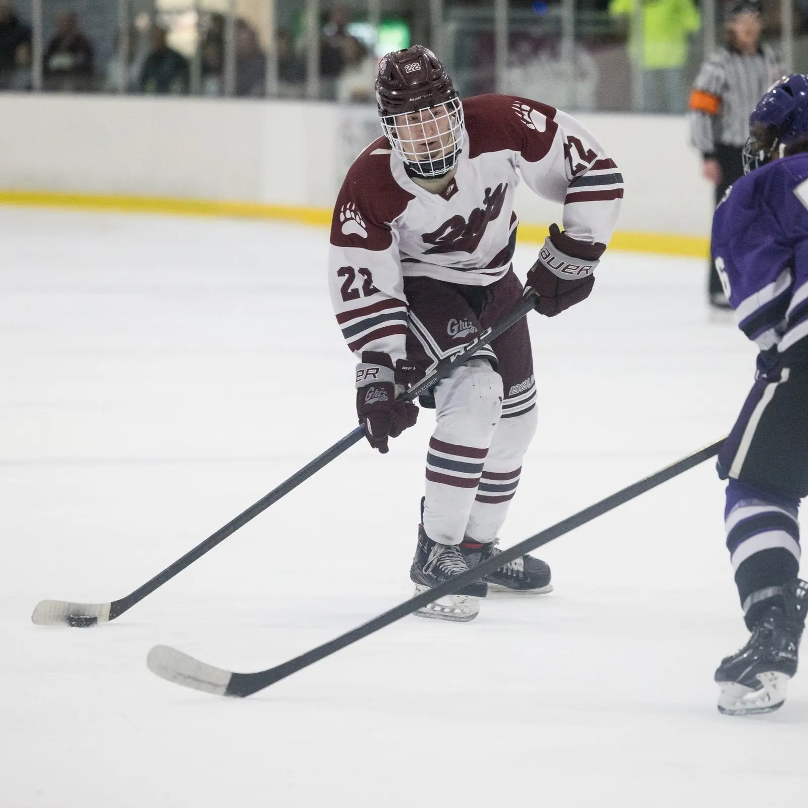 A hockey player in a maroon and white uniform skates across the ice during a game.
