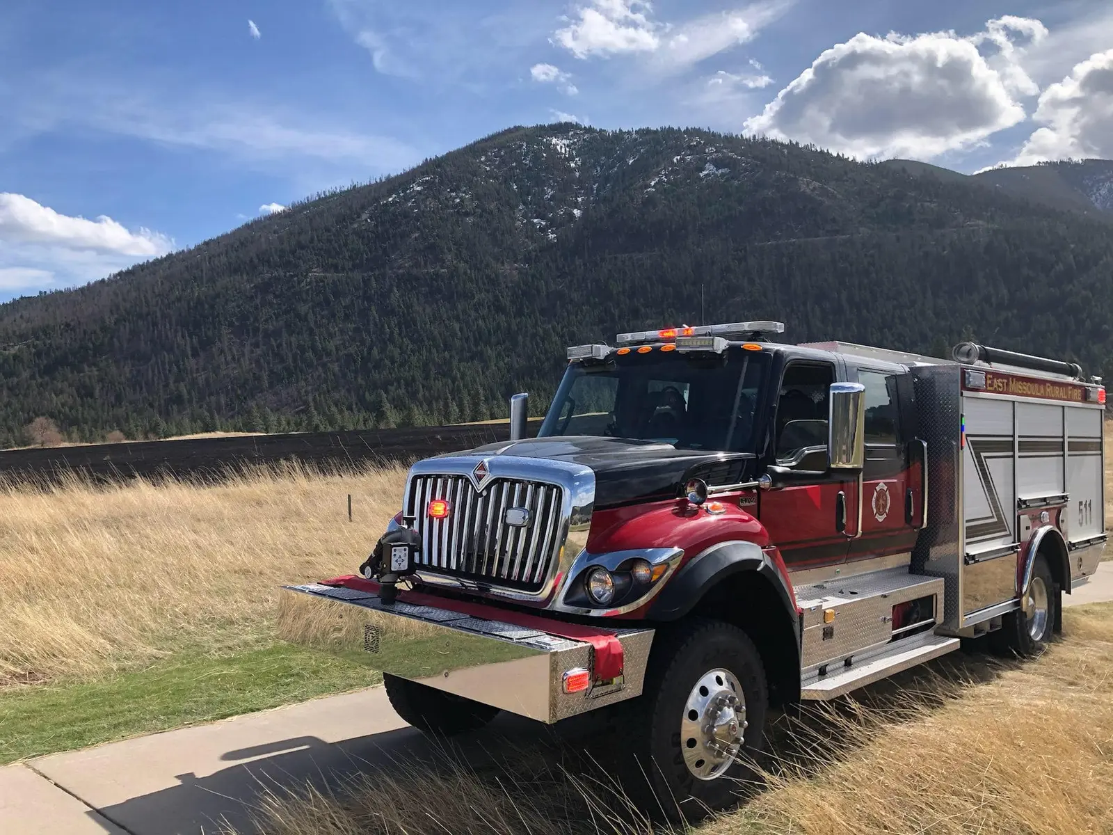 A fire truck is parked on a paved path in front of a mountain landscape.