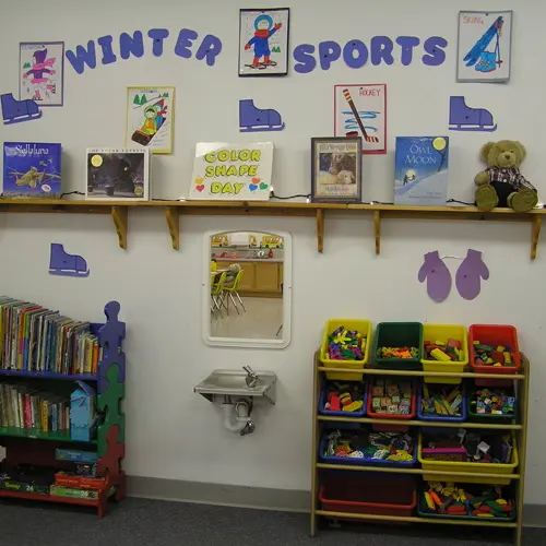 A decorated wall in a classroom features educational materials, books, and storage for toys.