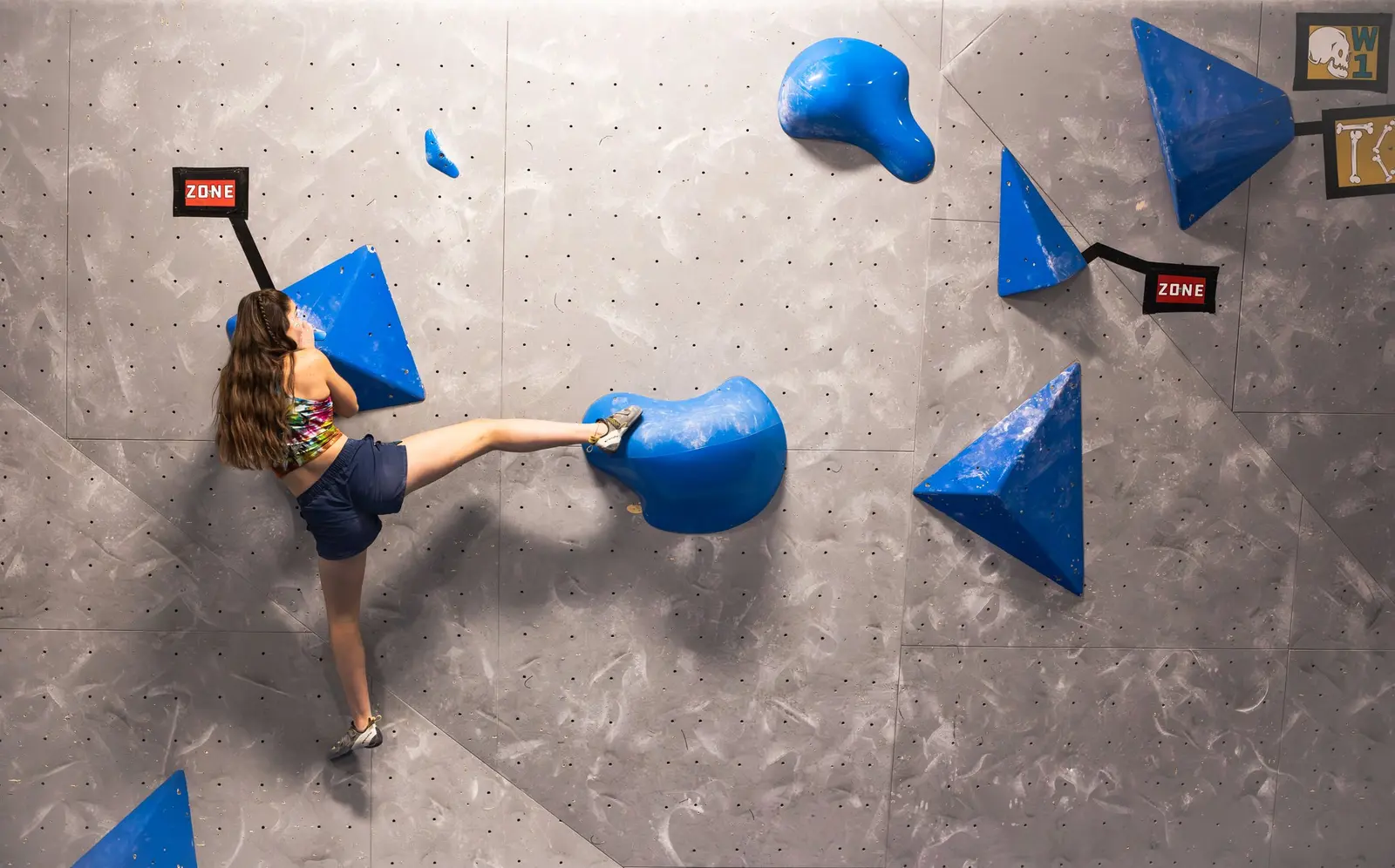 A young climber ascending an indoor bouldering wall with blue holds.