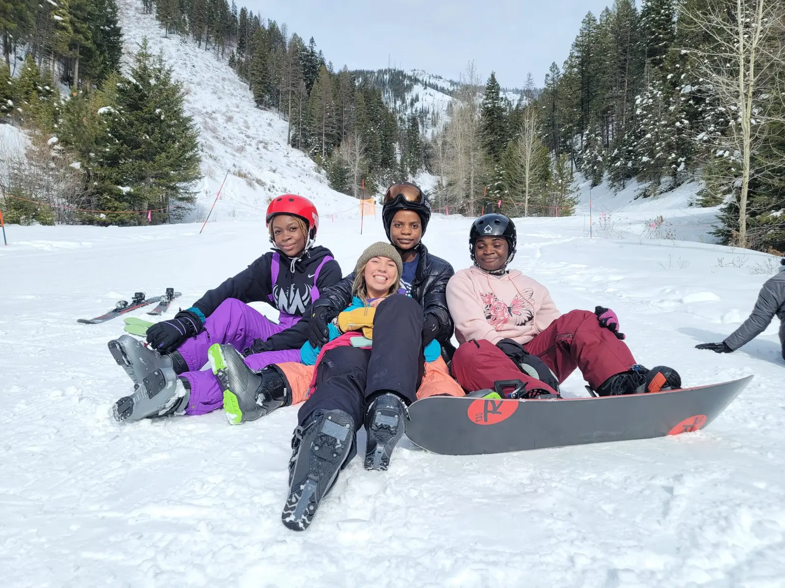 A group of four friends sitting together in the snow at a ski resort.
