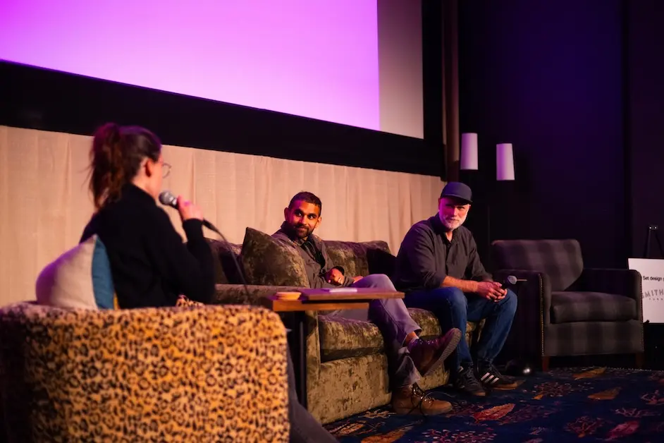 A woman interviews two men sitting on a couch on a stage.