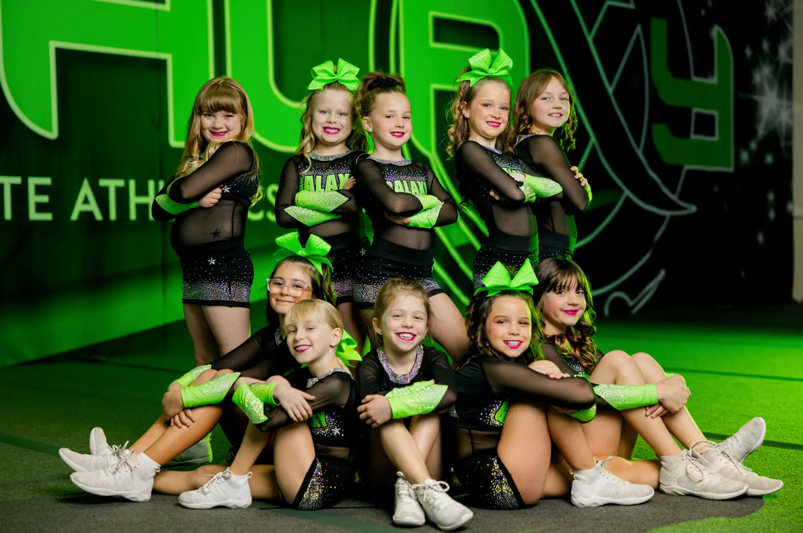 A group of young cheerleaders in matching black and neon green uniforms poses for a portrait.