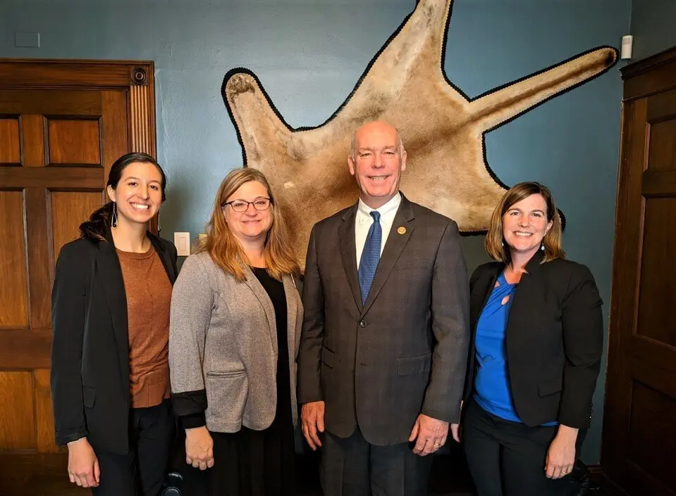 a group of three women and a man standing and smiling