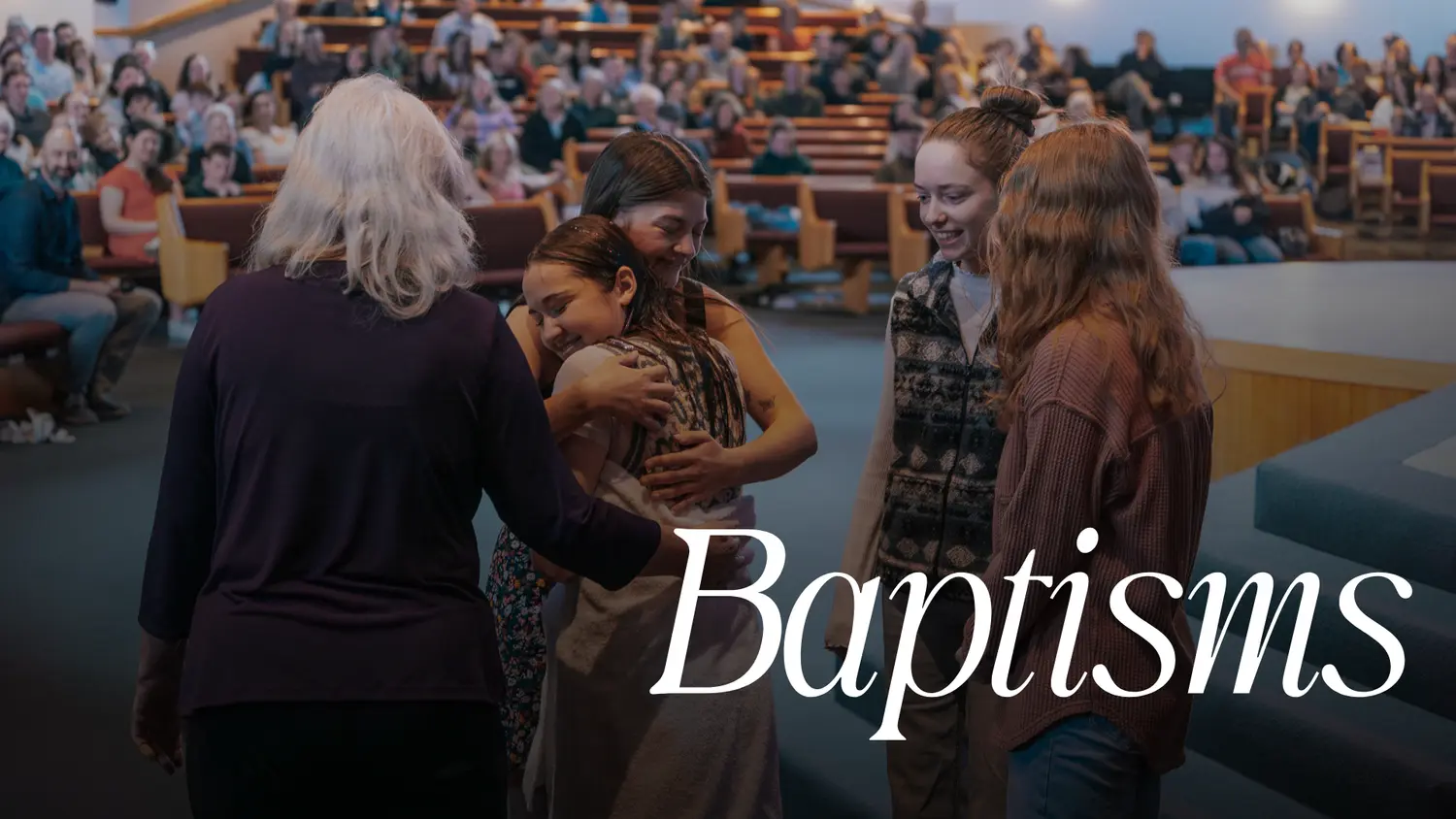A woman embraces a person who has just been baptized while others look on in a church.