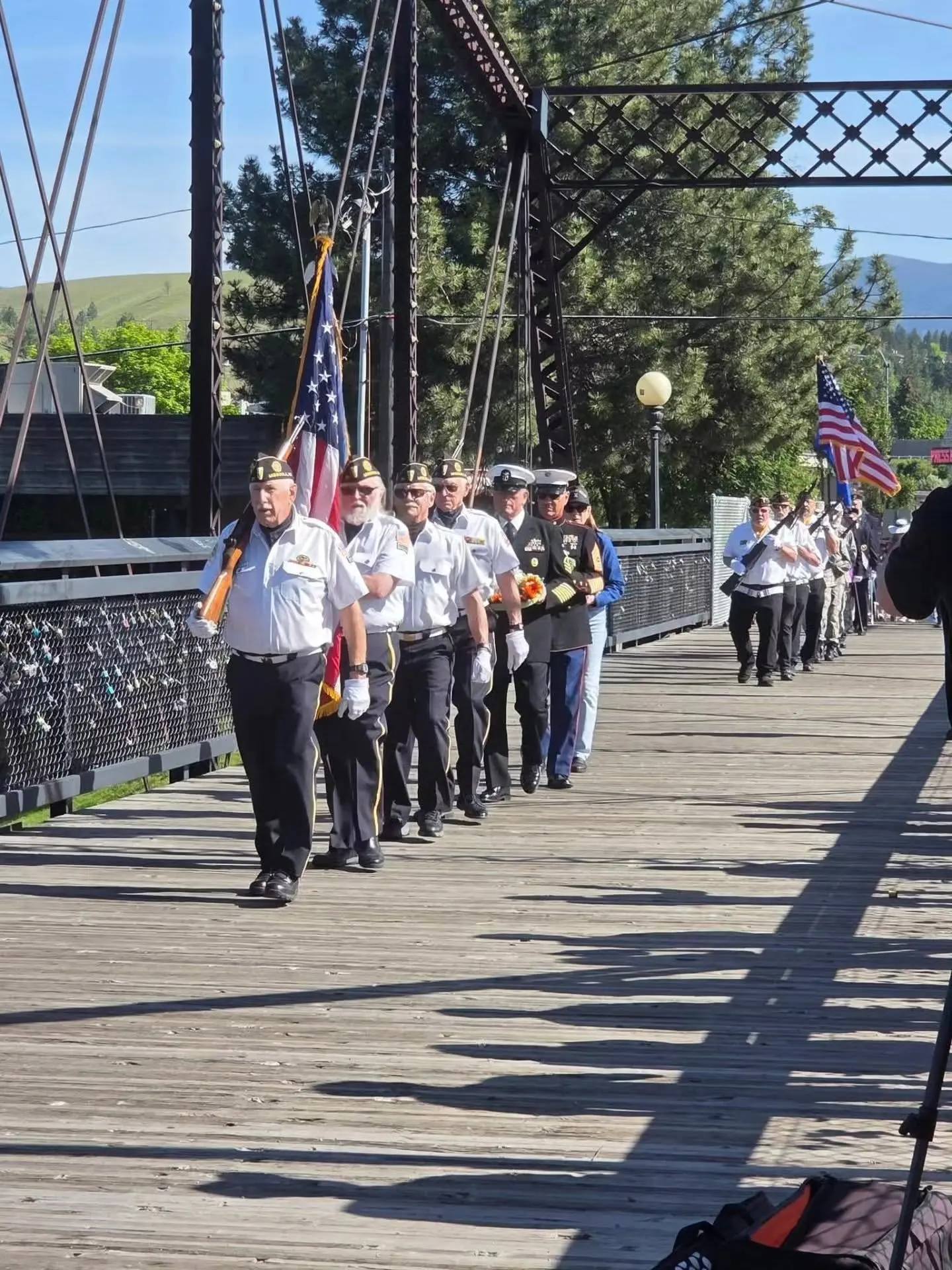 A group of veterans in uniform marches in formation across a wooden bridge.
