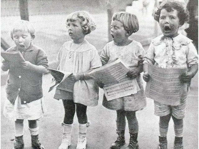 Four young children standing together, each holding a book, on a city street.