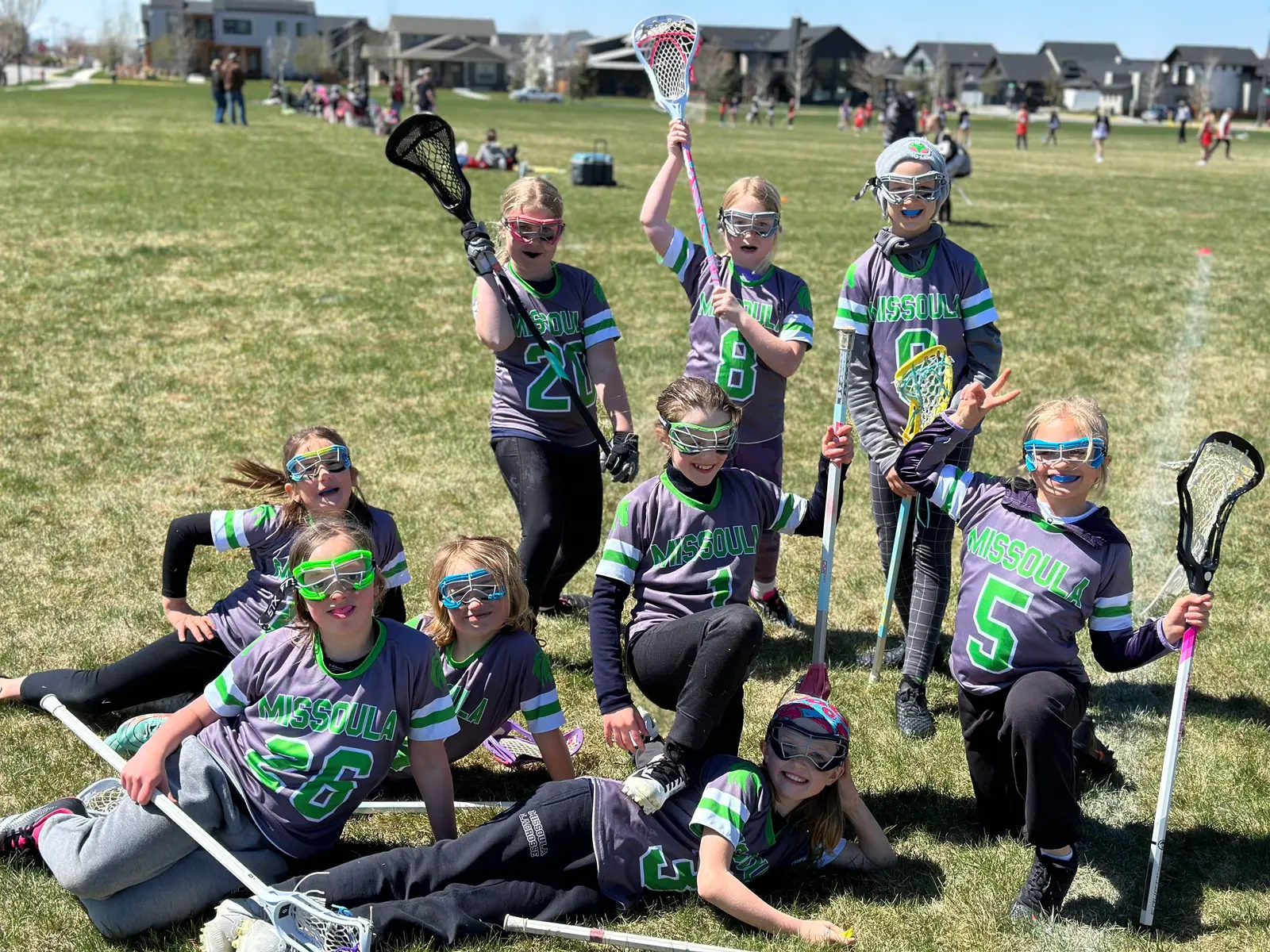 A group of young girls in lacrosse uniforms posing on a grassy field.