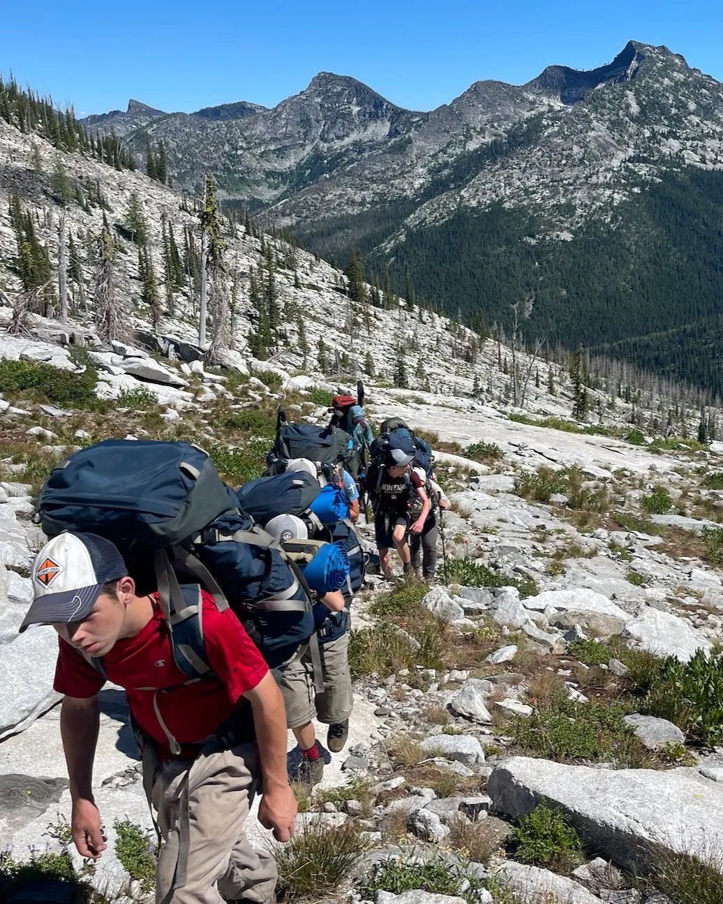 A group of hikers with large backpacks traverses a rocky mountain trail.