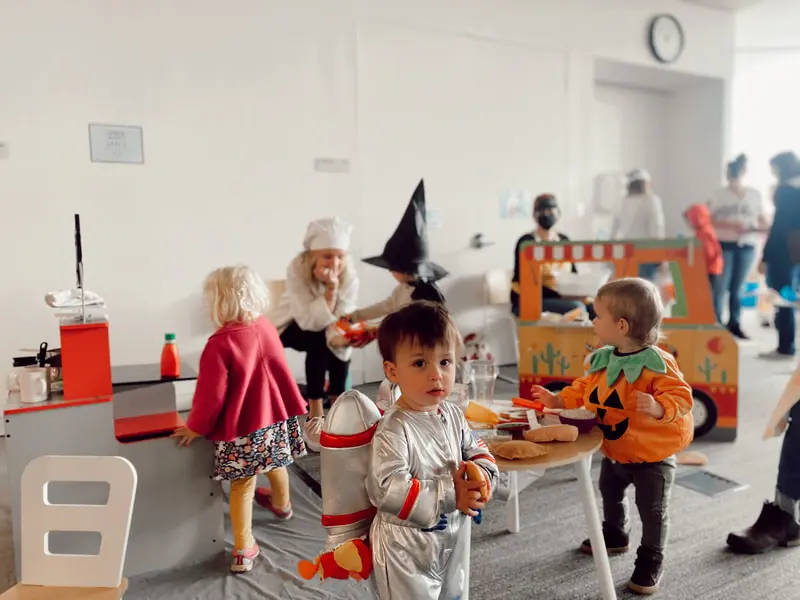 Young children wearing Halloween costumes play in an indoor activity area.