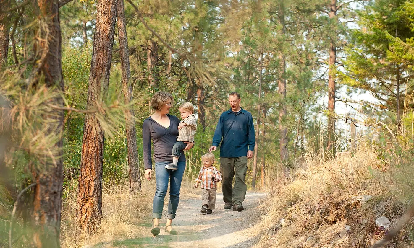 A family walks together on a wooded dirt trail.