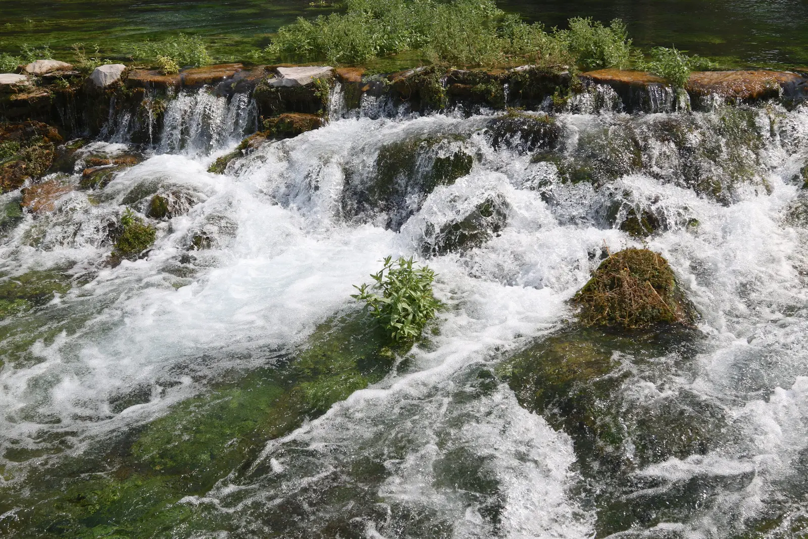 A small, rocky waterfall flows into a clear, green stream.