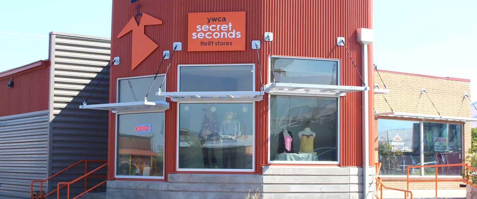 The exterior of a storefront for a thrift store with red metal siding and mannequins in the windows.