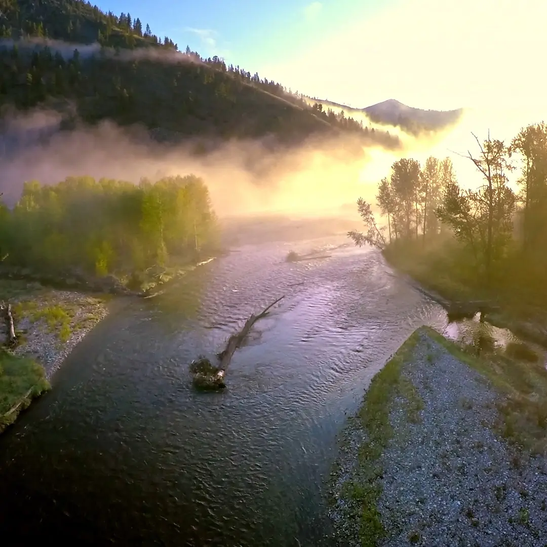 A river flows through a misty mountain valley at sunrise.