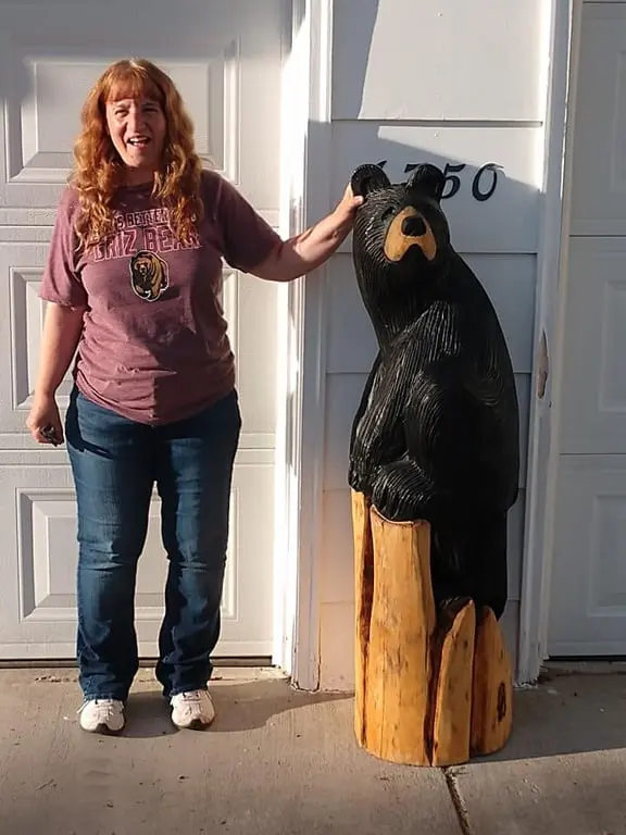A woman stands next to a wooden carved bear statue in front of a white garage door.