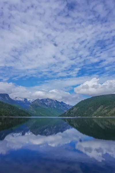 Photo from fs.usda.gov A calm lake reflects the surrounding forested mountains and cloudy sky.