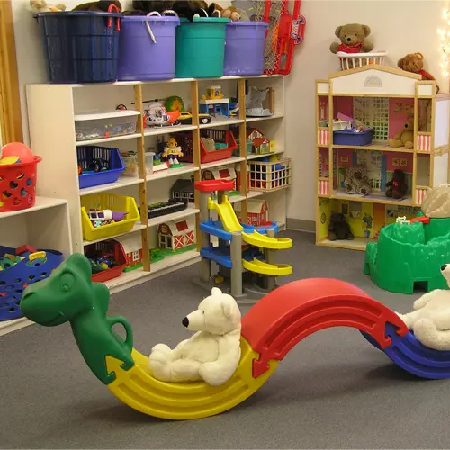 A brightly lit playroom is filled with various toys, storage bins, and a modular climbing structure.