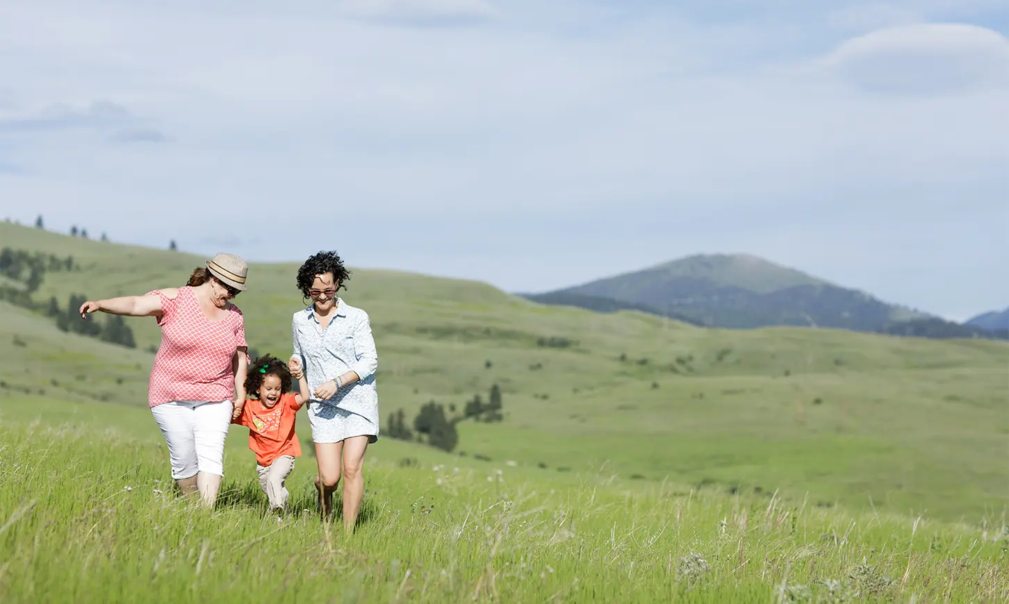 Two women and a young child walk together through a grassy field.