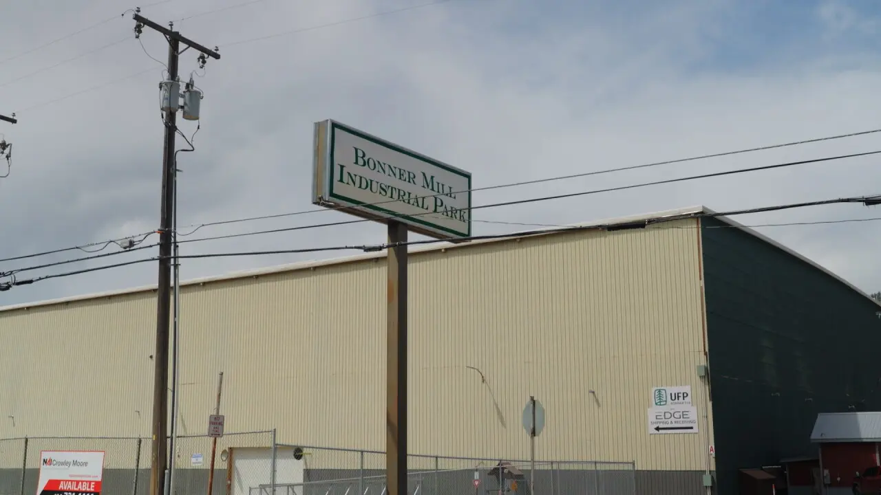 A sign for an industrial park stands in front of a large warehouse building.