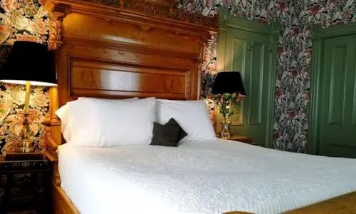 A view of a bedroom interior featuring a large wooden bed and floral wallpaper.