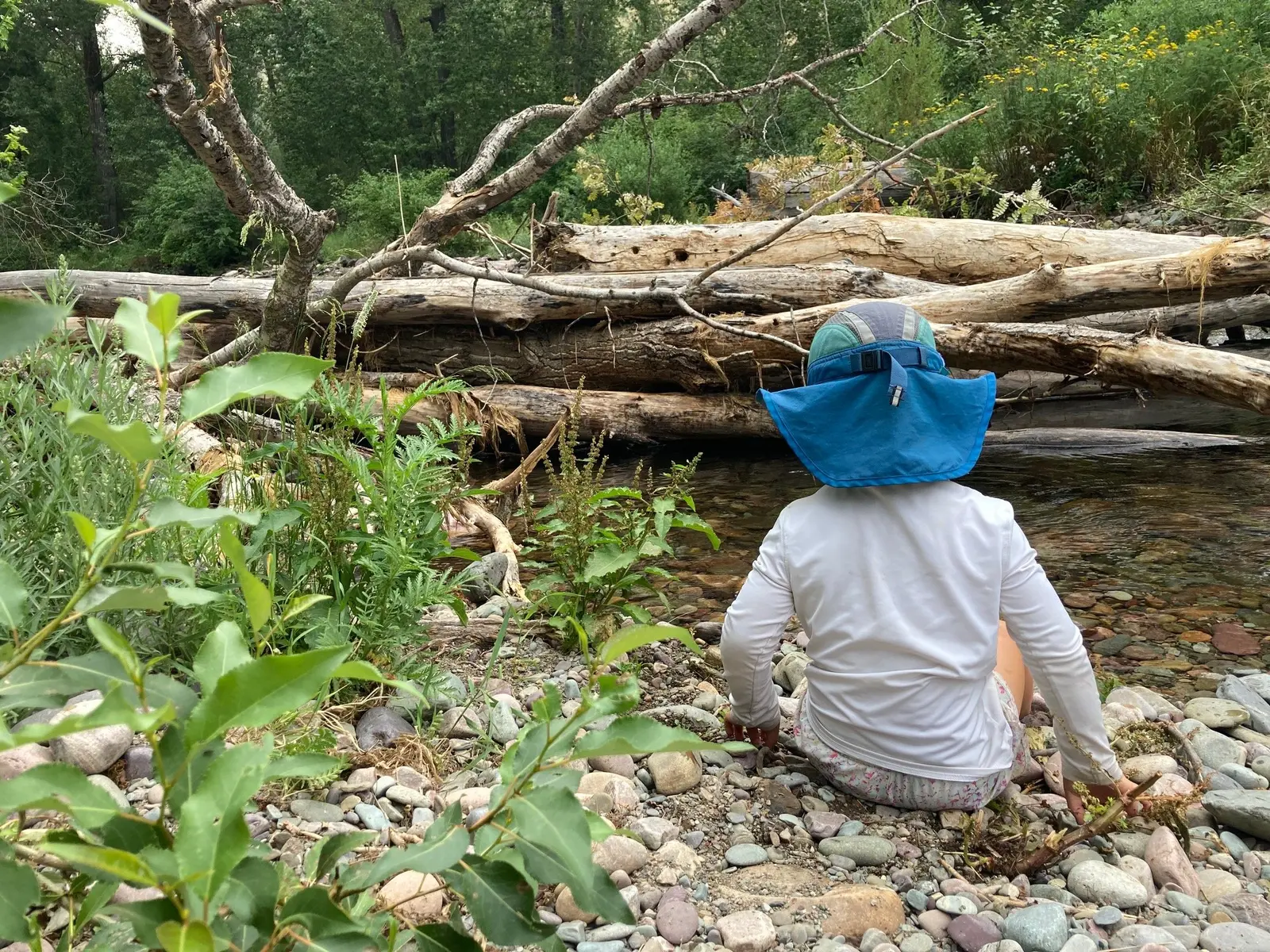A child wearing a sun hat sits on the rocky bank of a stream.