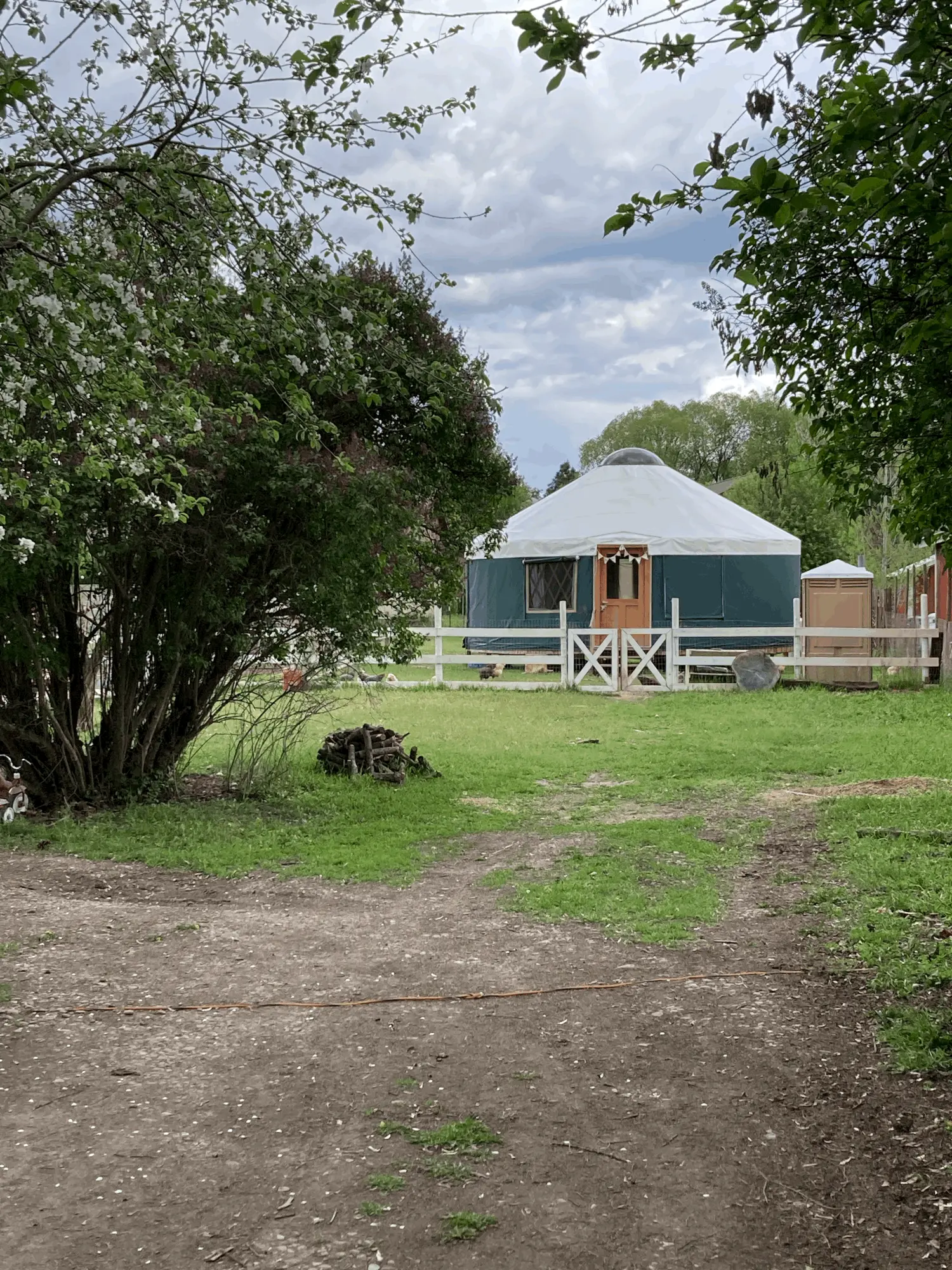 A yurt stands in a green field behind a white wooden fence.