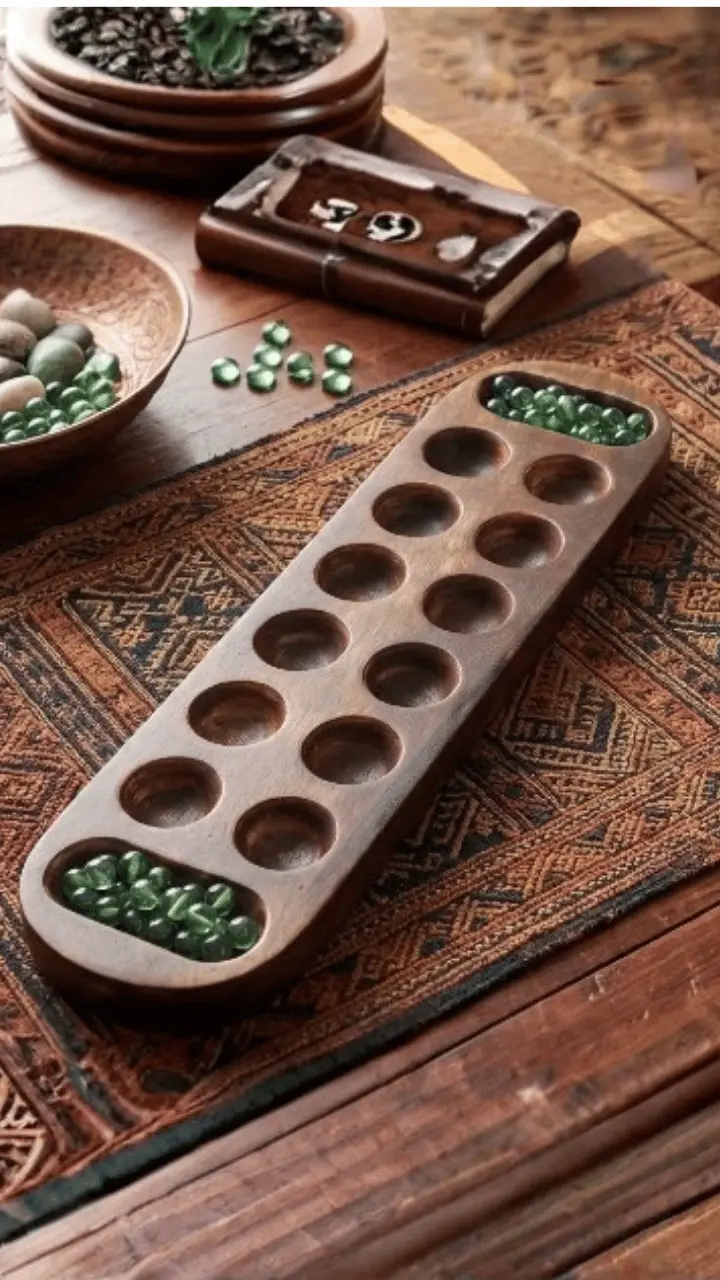 A wooden mancala board with glass marbles sits on a patterned runner.