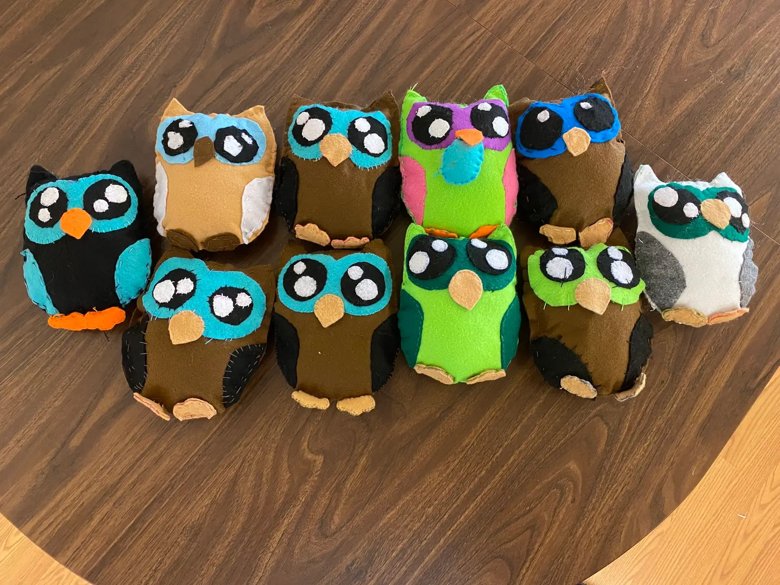 A collection of handmade felt owl plushies sits on a wooden table.