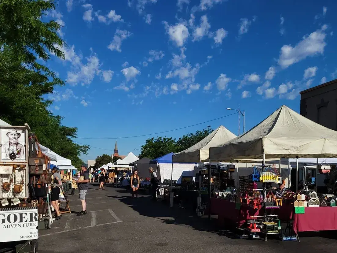 A street market with vendors under white tents on a sunny day.