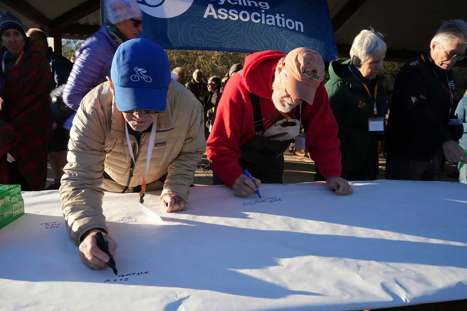 Adults stand at a table writing on a large white paper banner.
