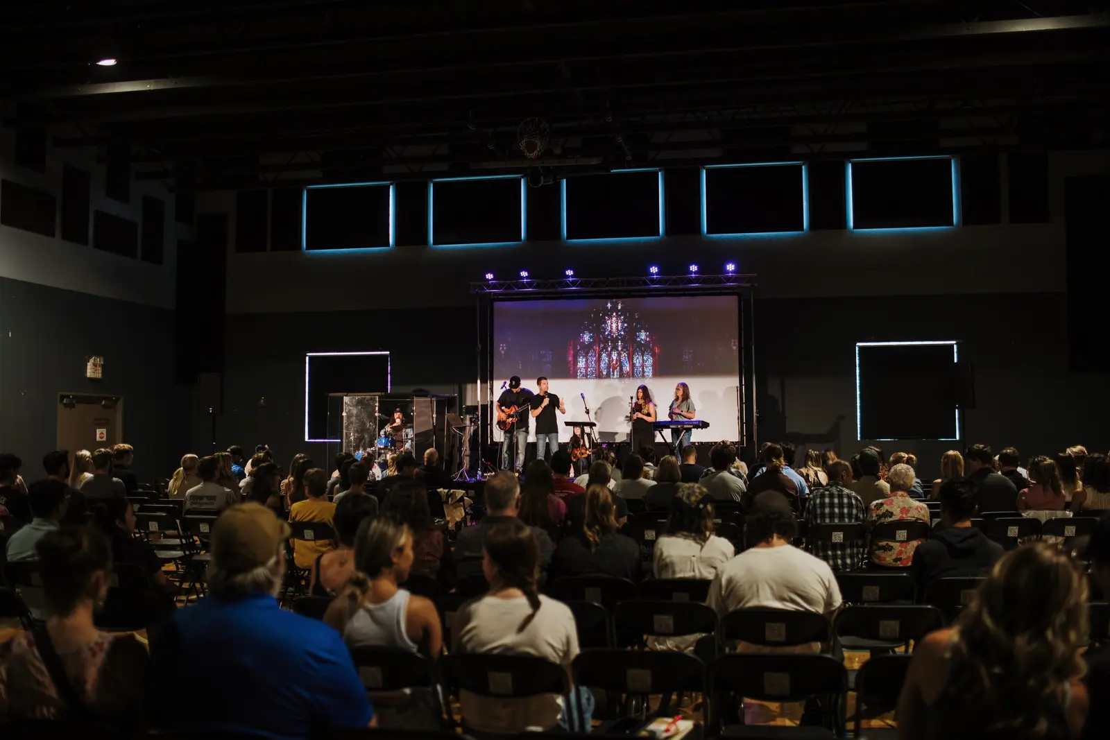 A musical performance takes place on a stage before a large audience in a dimly lit auditorium.