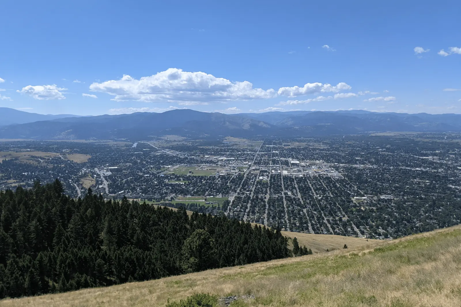A high-angle view captures a city nestled in a valley beneath mountain ranges.