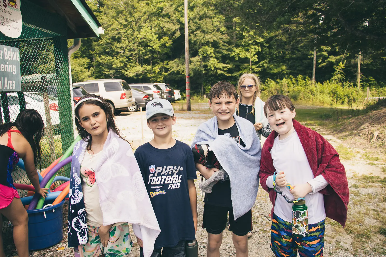 A group of children wrap themselves in towels outdoors after swimming.