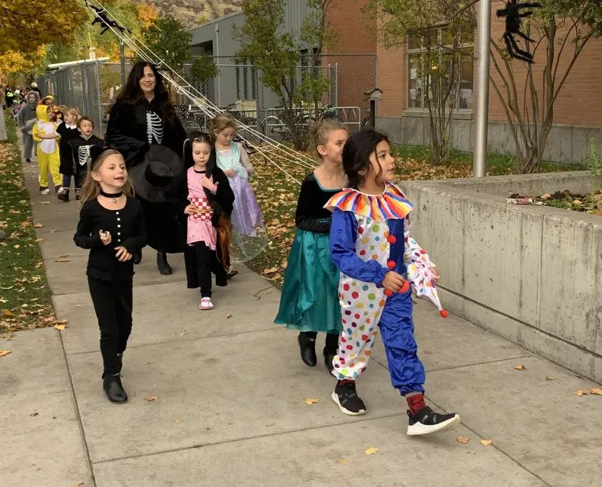 A group of children in Halloween costumes walk along a sidewalk.
