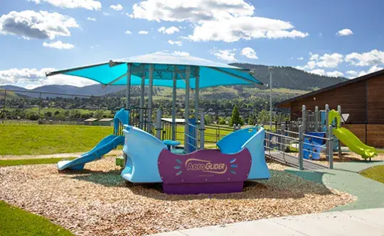 A colorful playground structure stands in a grassy park setting under a bright sky.