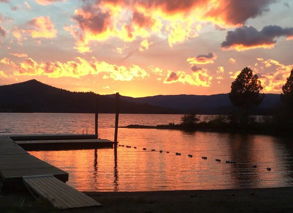 A wooden dock sits on a lake under a vibrant sunset sky.