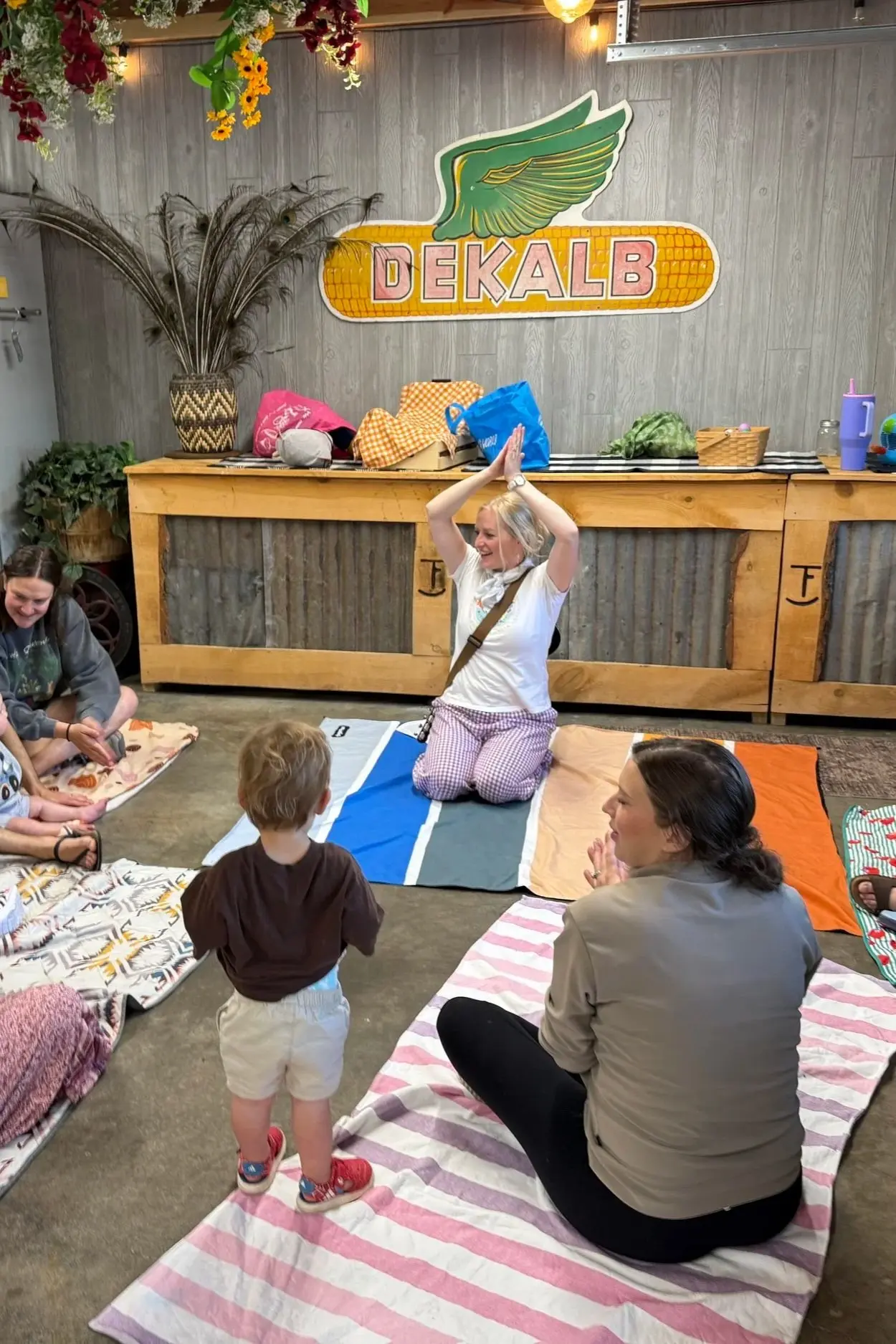 A group of adults and a child sit on blankets on the floor in an indoor space.