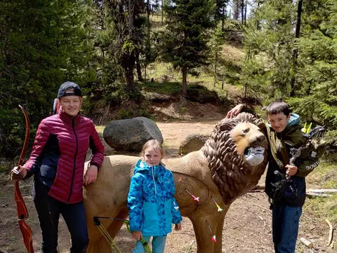 Three children pose with a lion archery target in a wooded area.