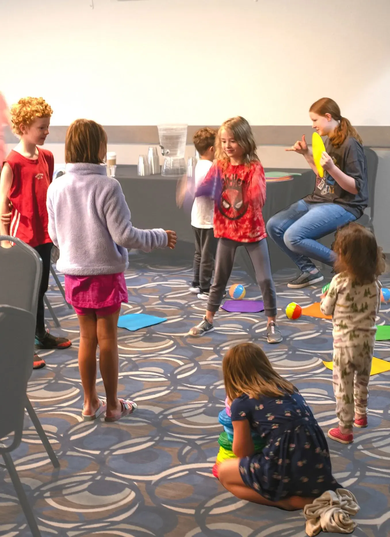 A group of children and a youth instructor are engaged in activities on a carpeted floor.