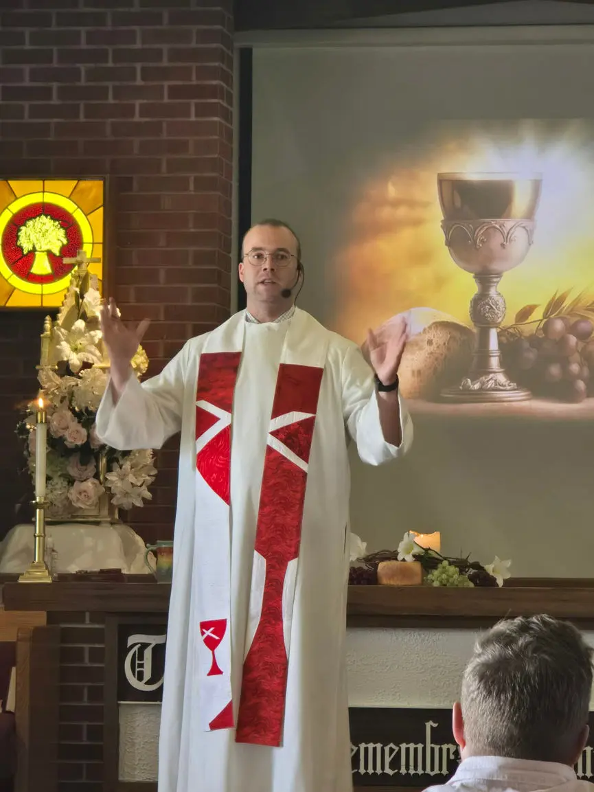 A man wearing religious vestments stands before a congregation and gestures while speaking.
