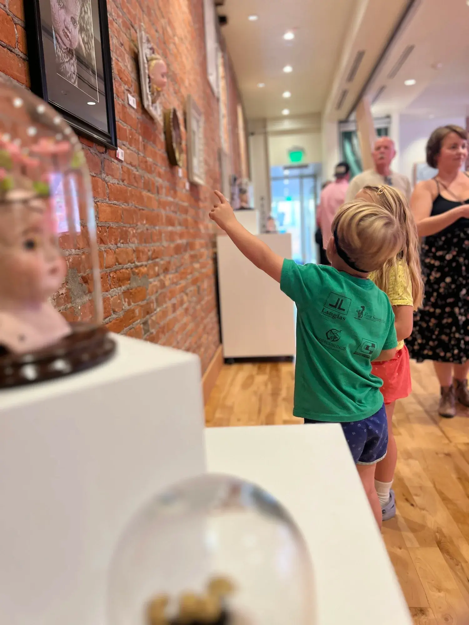 A child points at an artwork on a brick wall in a gallery space.