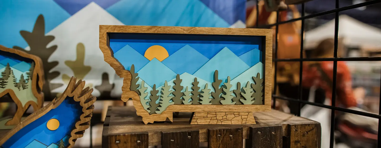 A layered wooden craft representing a mountain landscape sits on a wooden crate.